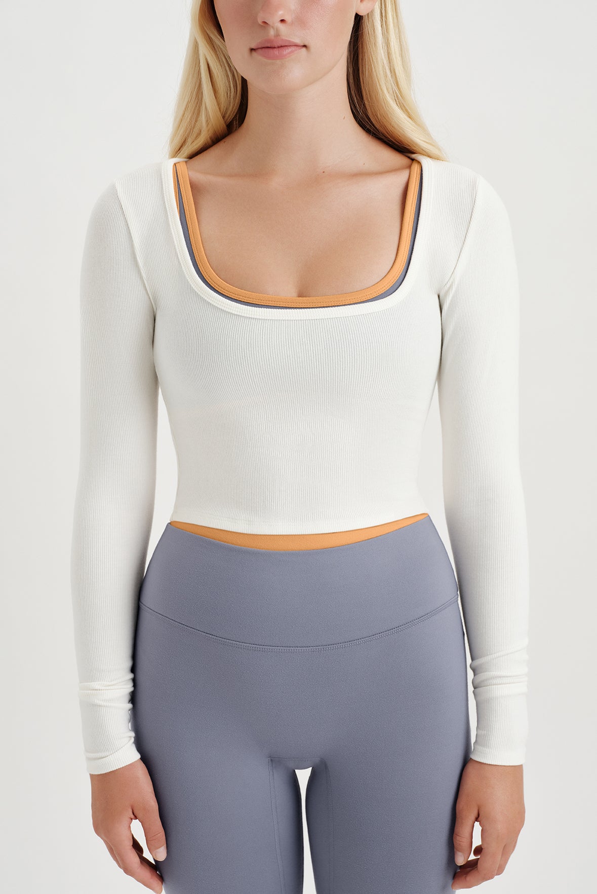 Person wearing a white long-sleeve top and purple leggings on a plain background