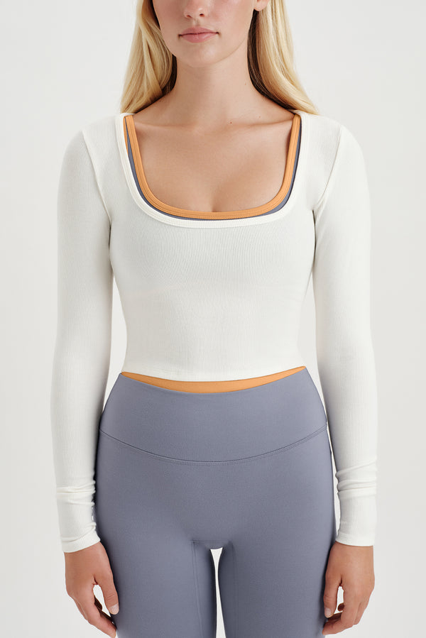 Person wearing a white long-sleeve top and purple leggings on a plain background