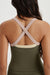 Person wearing a green tank top with criss-cross straps on a plain background