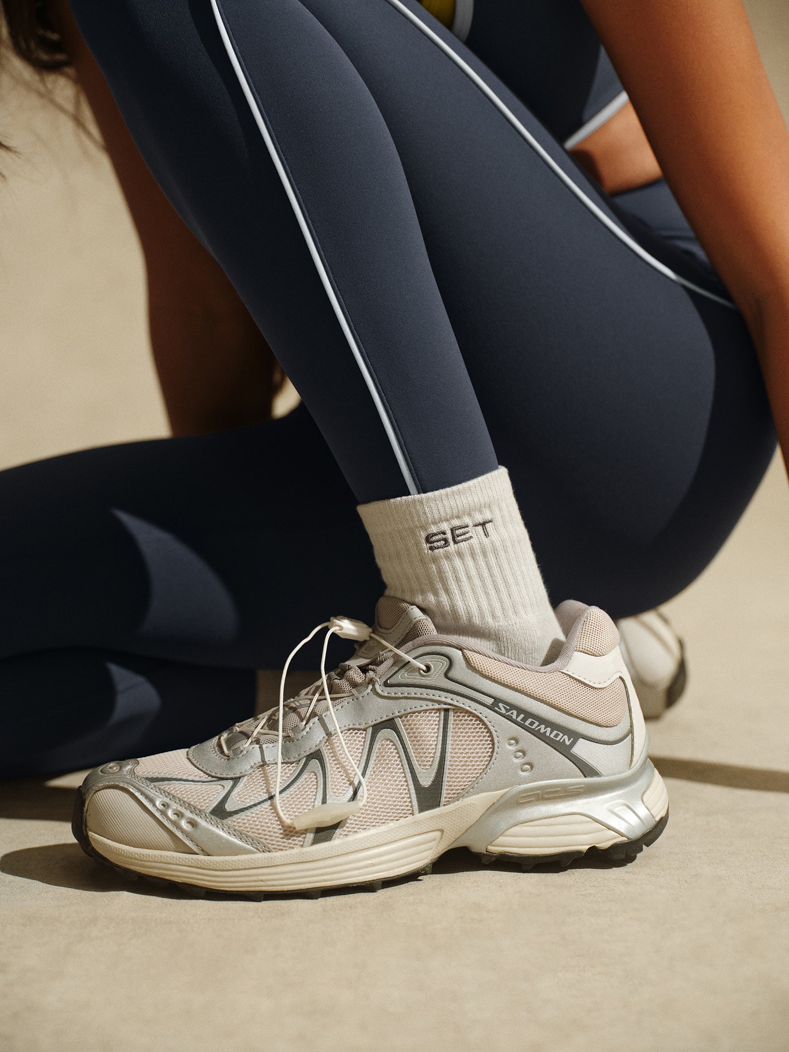 Close-up of a person wearing gray athletic shoes and dark leggings on a neutral background