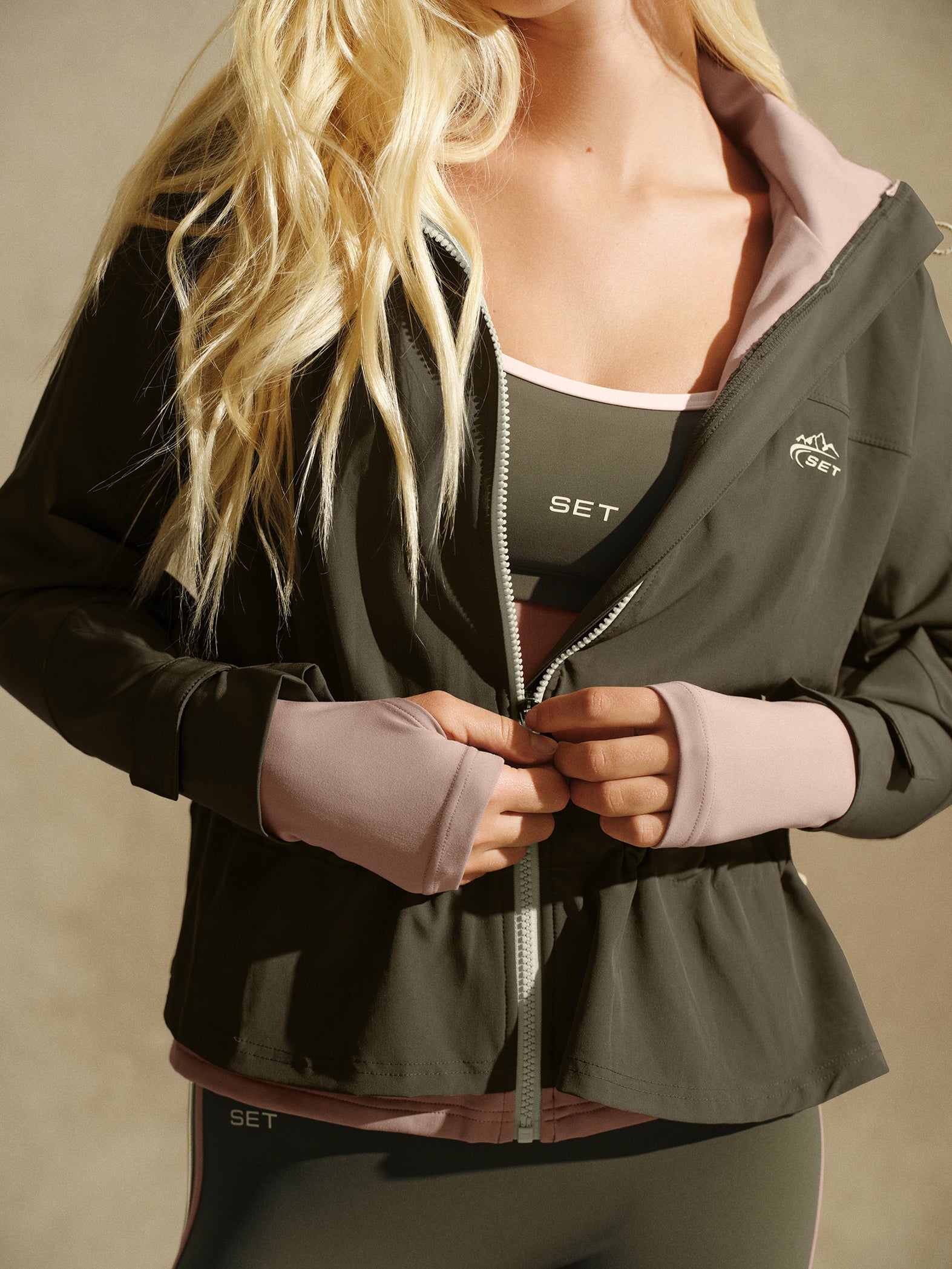 Close up of person wearing green and pink tracksuit on a beige background 
