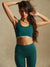 Woman wearing a green sports bra and leggings with a beige background