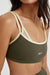 Green sports bra with beige straps worn by a person on a white background