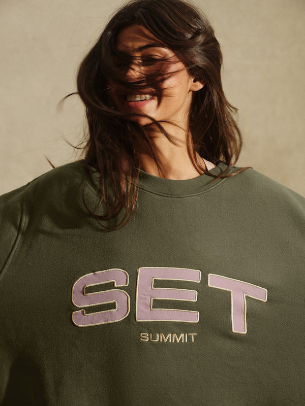 Person wearing a green sweatshirt with 'SET SUMMIT' text on a neutral background