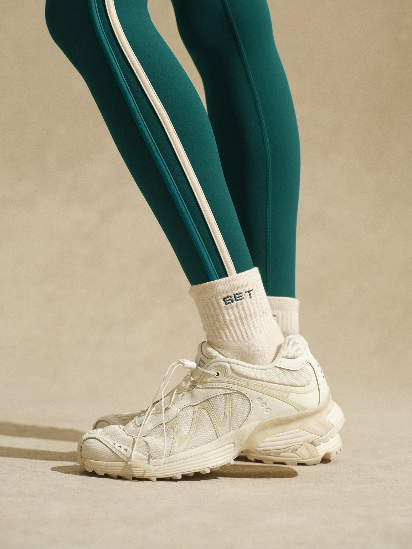 Teal leggings with white stripes and white sneakers on a beige background