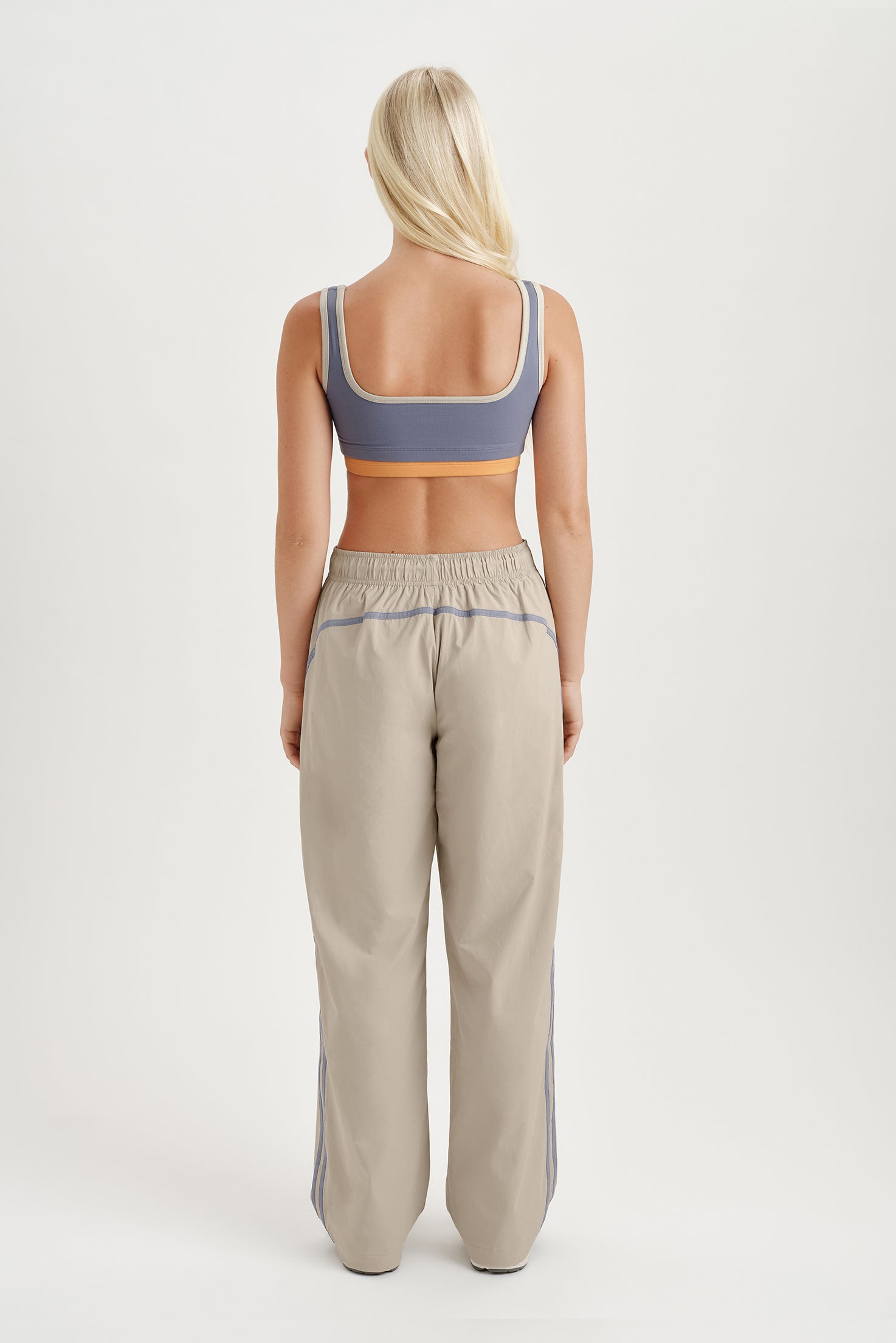 Person wearing a sports bra and track pants on a white background