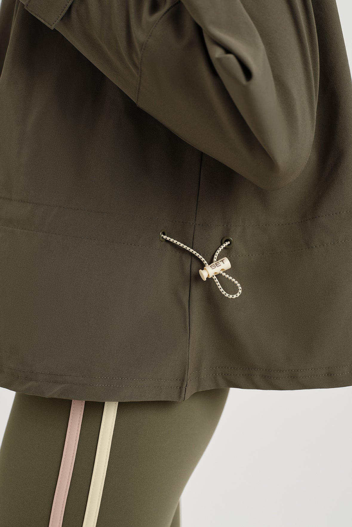 Close-up of a person wearing an olive green jacket with a hood, focusing on the drawstring detail.