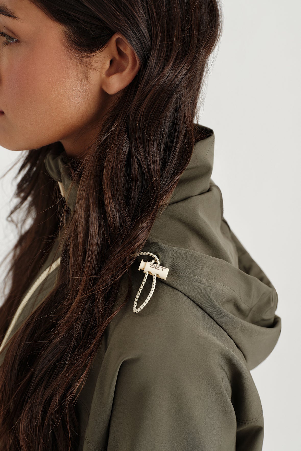 Close-up of a person wearing a green hooded jacket with a brand logo on a white background