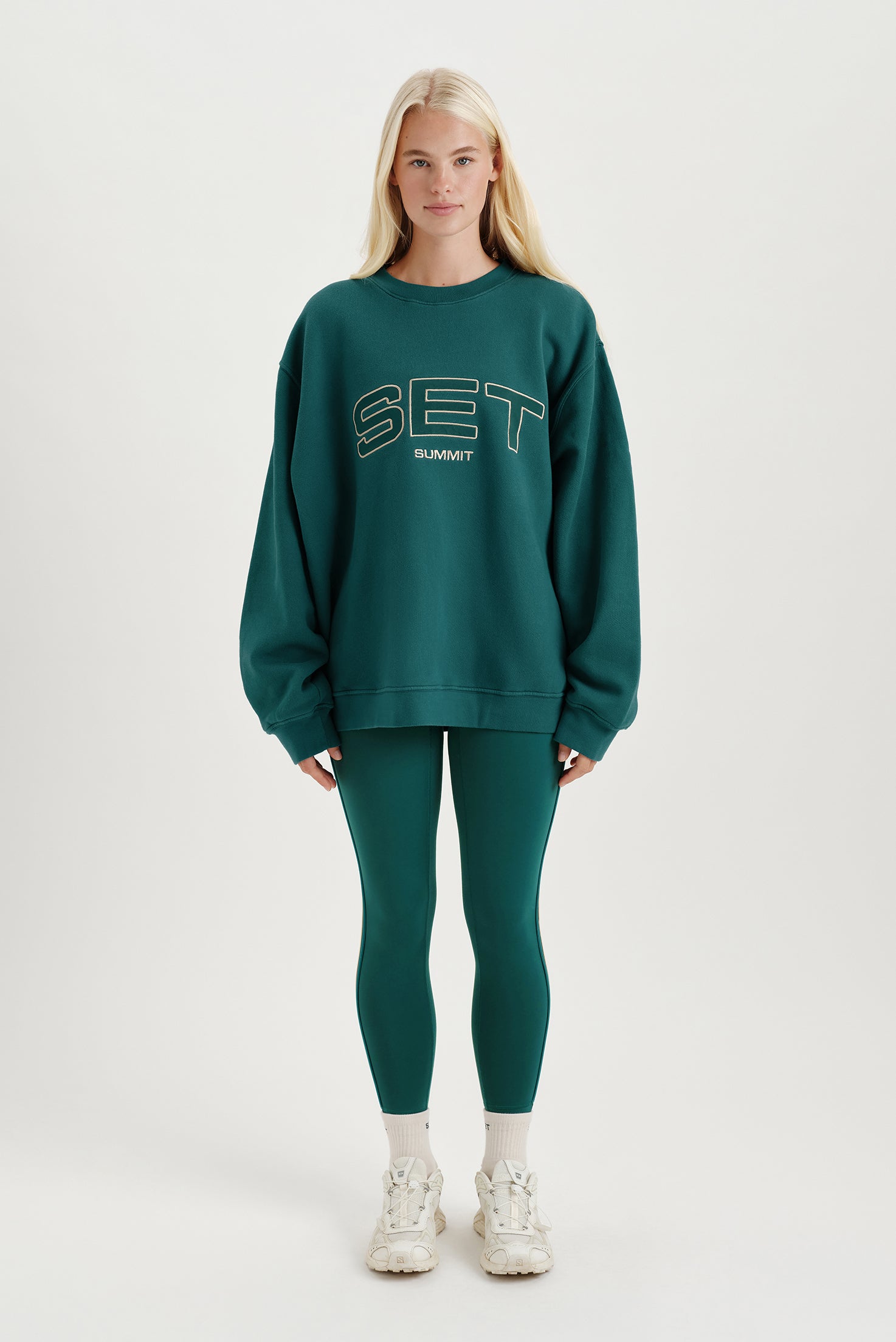 Person wearing a green 'SET' sweatshirt and leggings on a white background