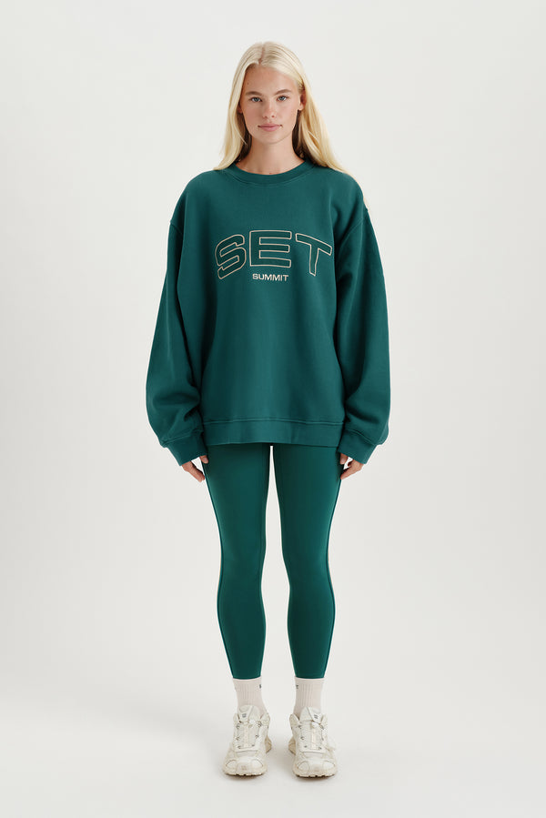 Person wearing a green 'SET' sweatshirt and leggings on a white background