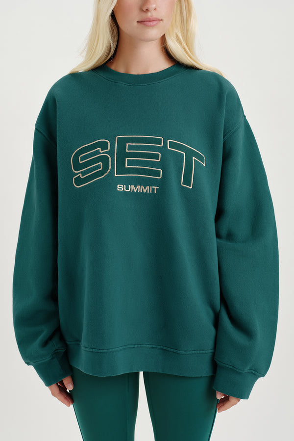 Person wearing a green sweatshirt with 'SET SUMMIT' text on a white background