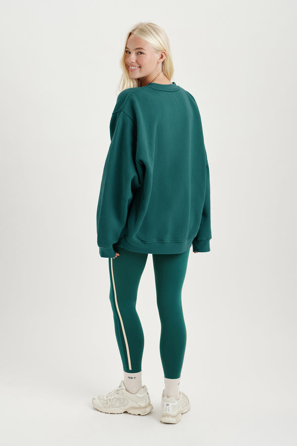 Woman wearing a teal sweatshirt and leggings with white sneakers on a white background