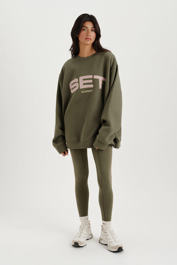 Person wearing a green 'SET' sweatshirt and leggings on a white background 
