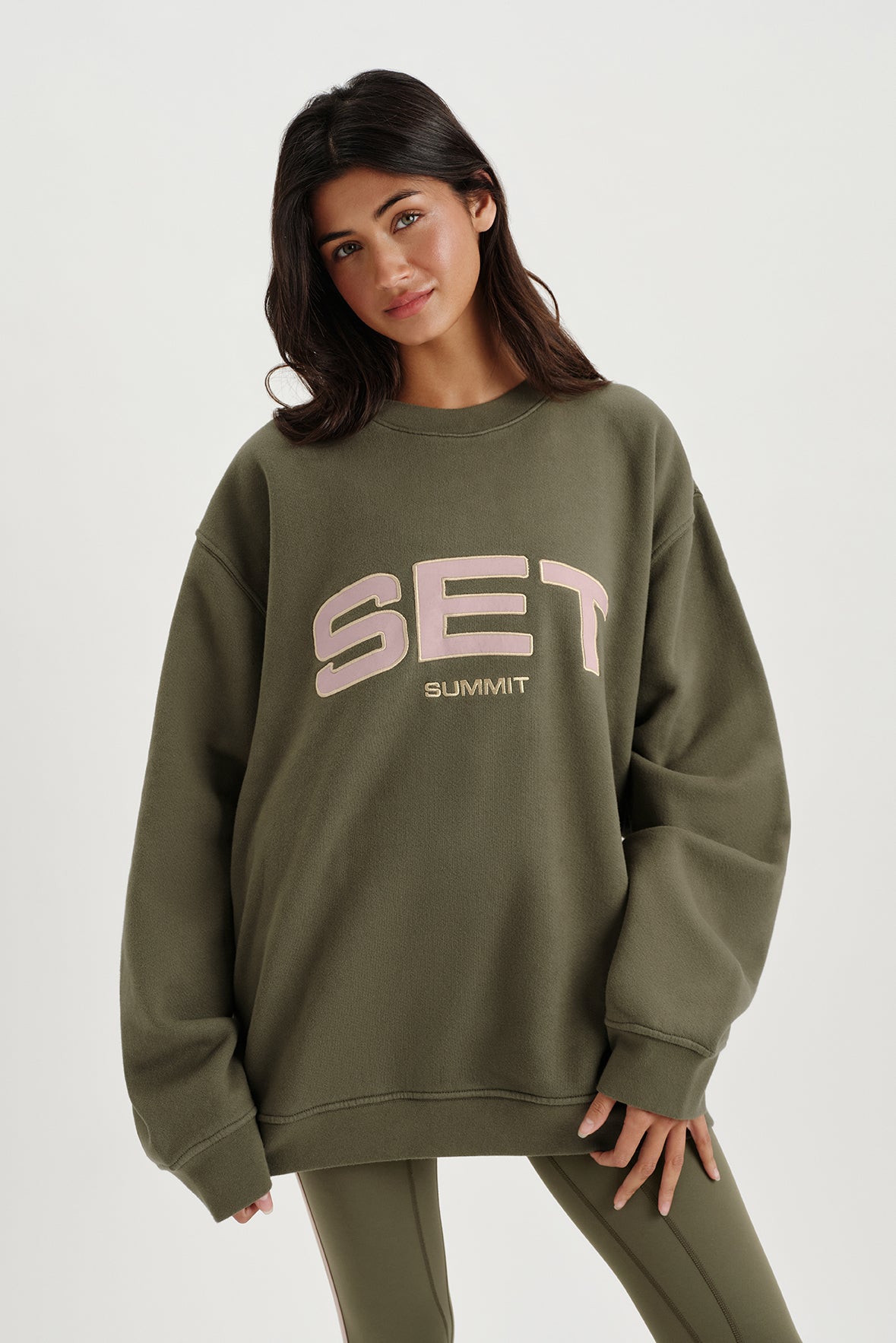 Woman wearing an olive green sweatshirt with 'SET' logo on a white background