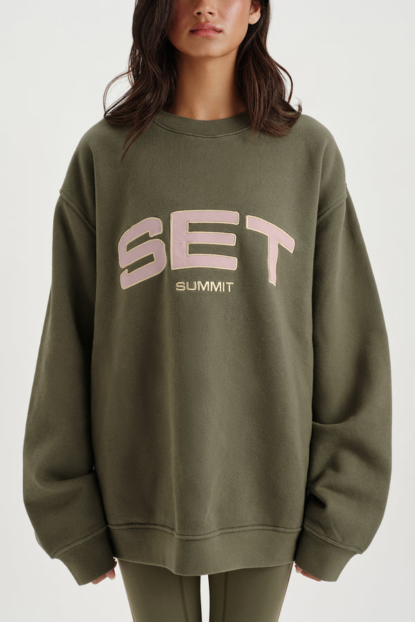 Person wearing a green sweatshirt with 'SET SUMMIT' text on a white background