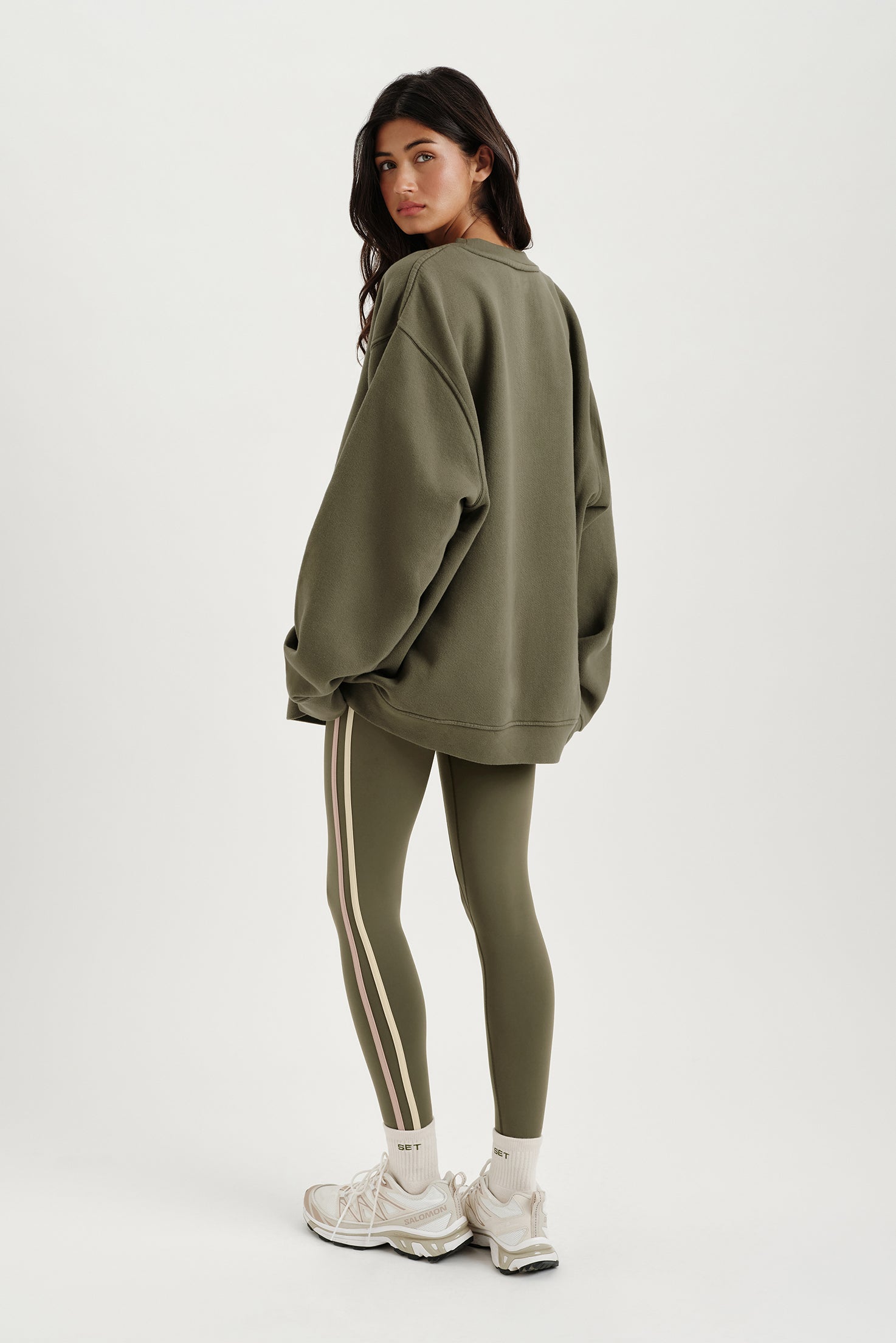 Person wearing an olive green oversized sweatshirt and leggings with white sneakers on a white background