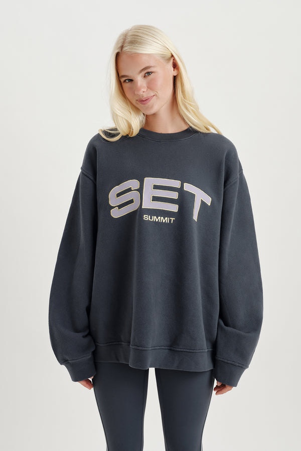 Person standing wearing a grey sweatshirt with 'SET' logo  