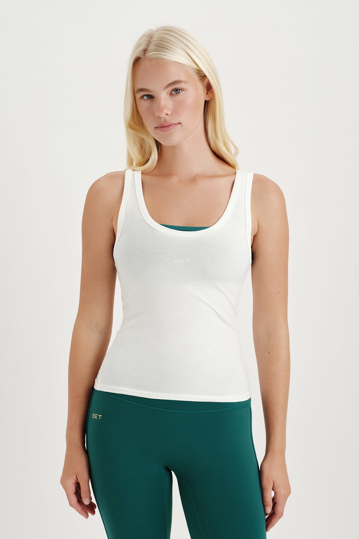 Woman wearing a white tank top and green leggings on a light gray background <model-info>Kathryn wears a size S and is 5’8½ , 24” waist, 33B bust.</model-info> 