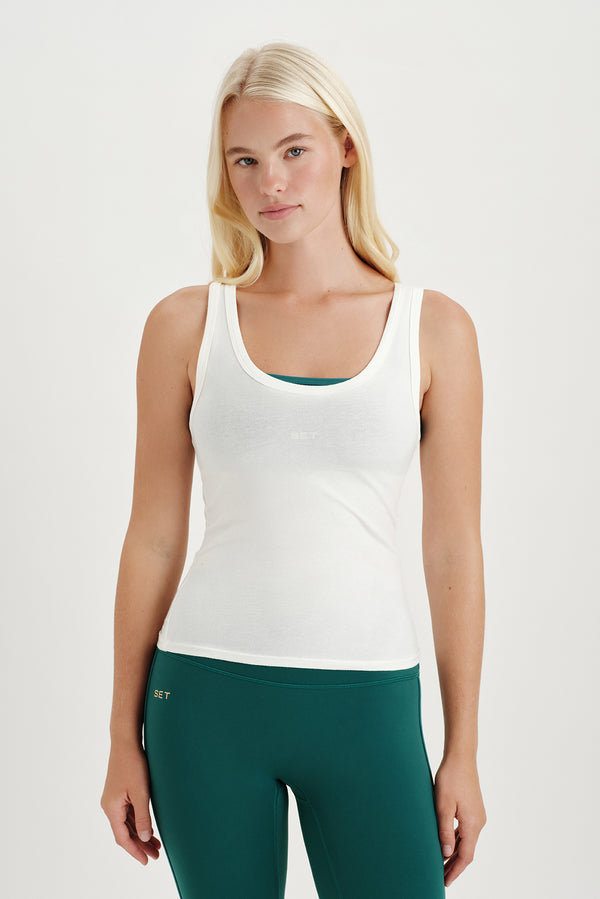 Woman wearing a white tank top and green leggings on a light gray background 
