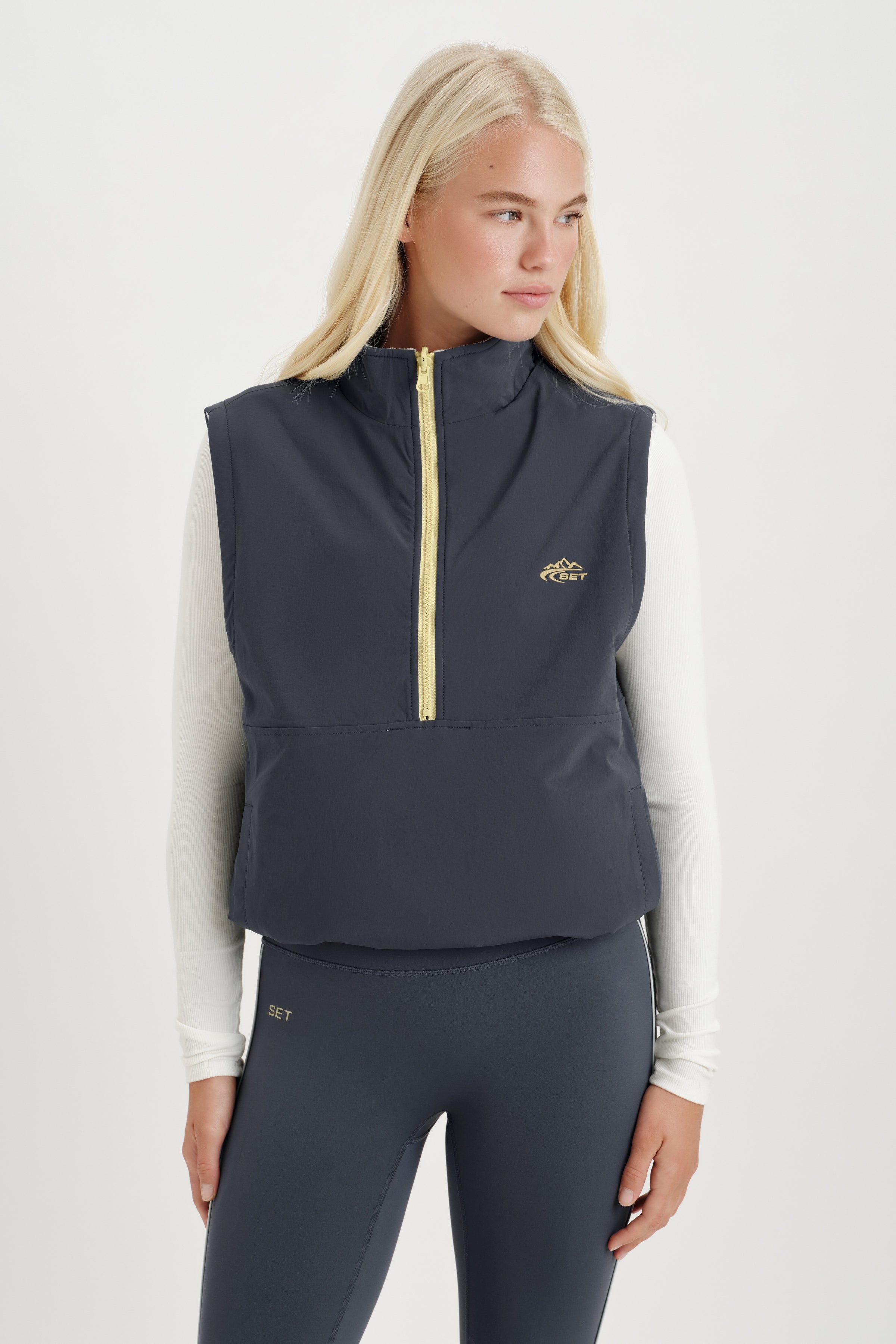 Woman wearing a gray vest with a white long sleeve on a white background 