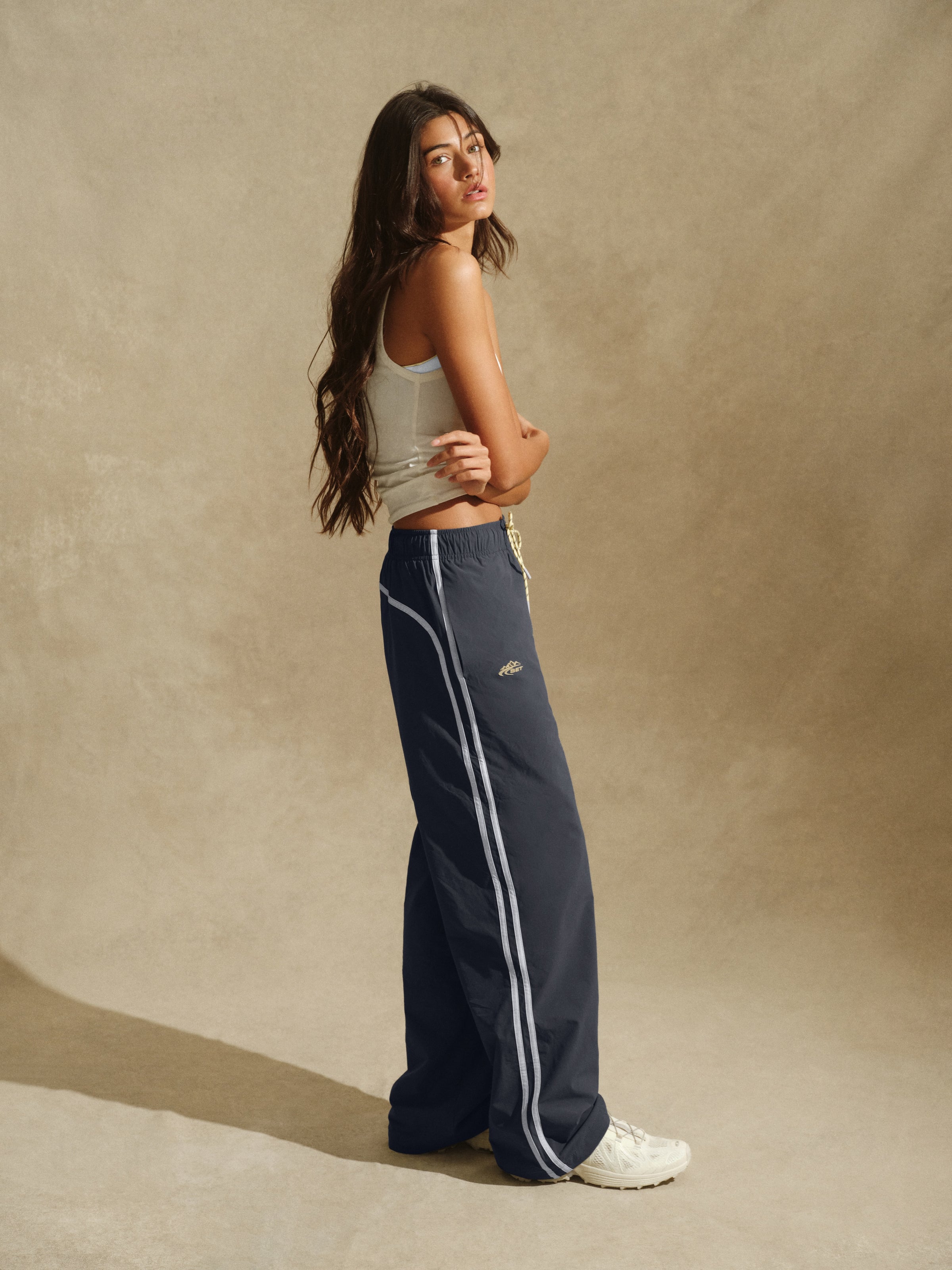 Person standing with white tank top and gray track pants with stripes 