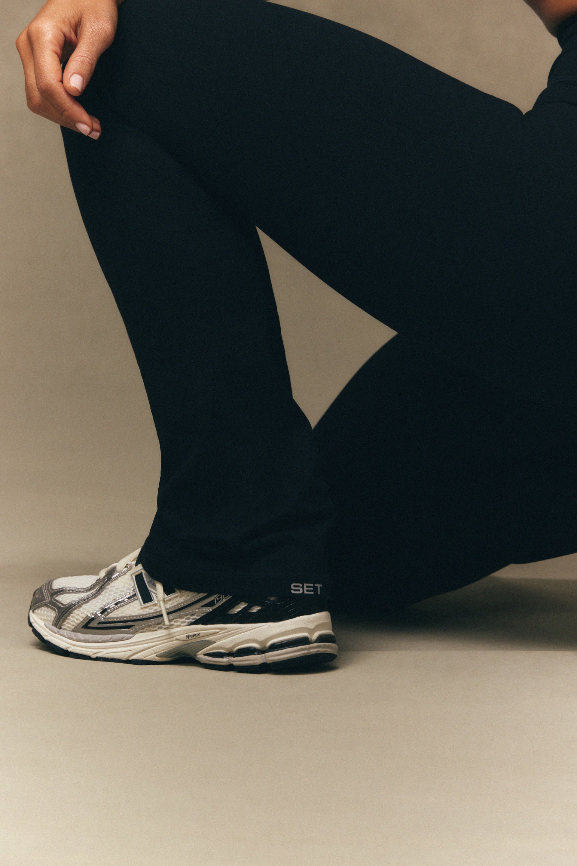 Person wearing black pants and a white athletic shoe on a neutral background