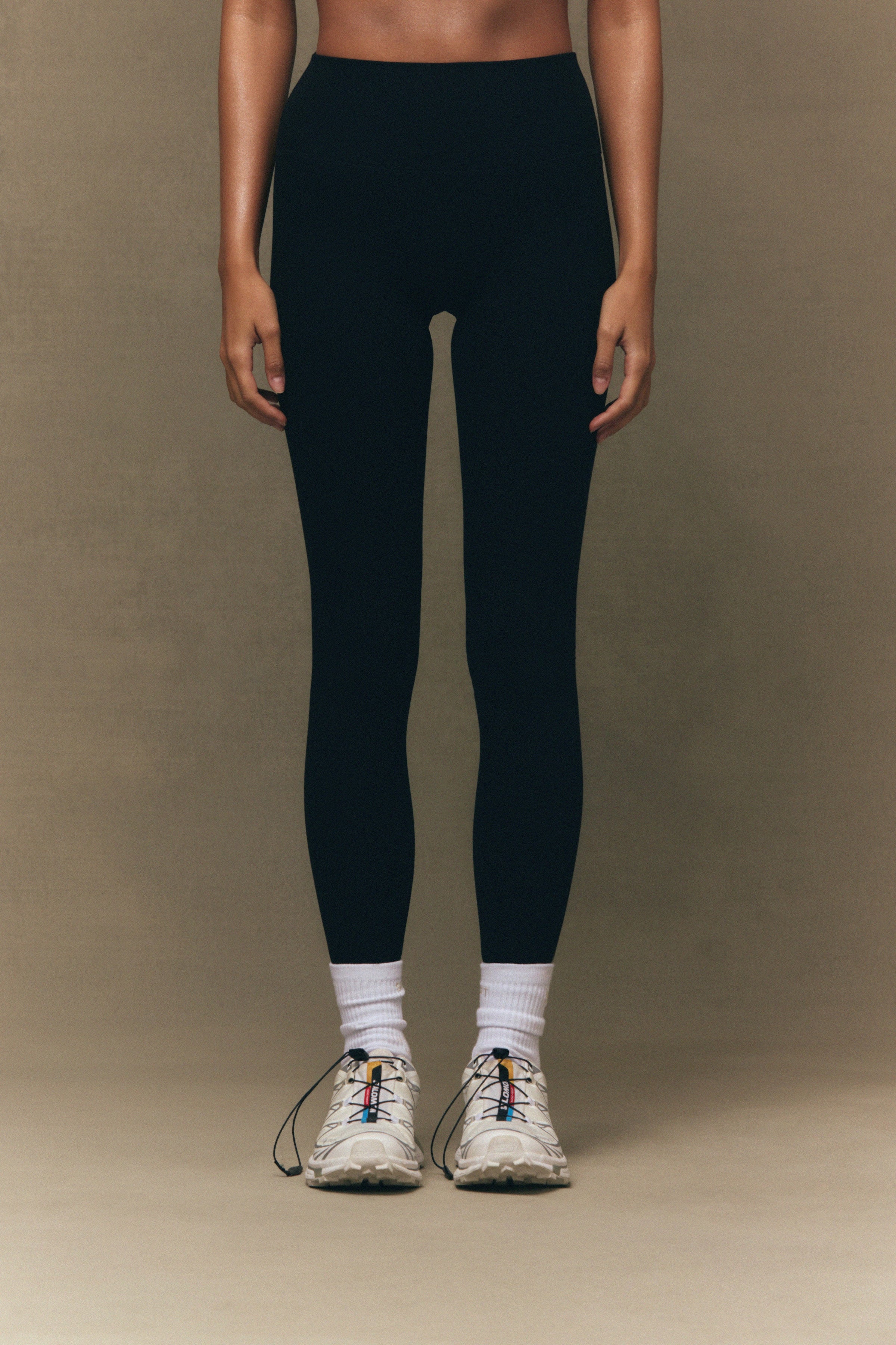 Person wearing black leggings and white sneakers on a brown background 