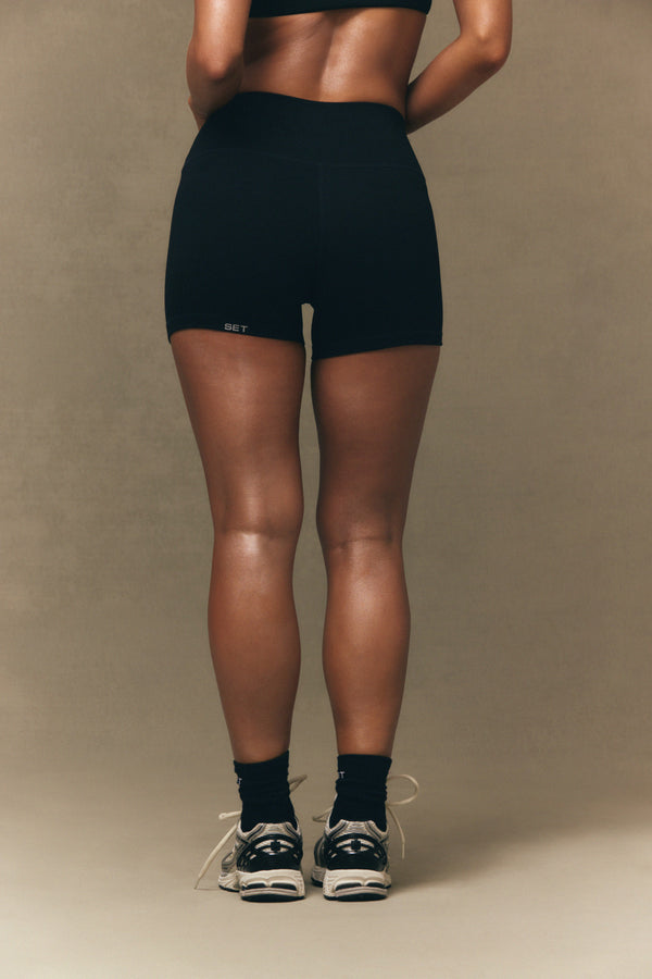 Person wearing black athletic shorts on a beige background