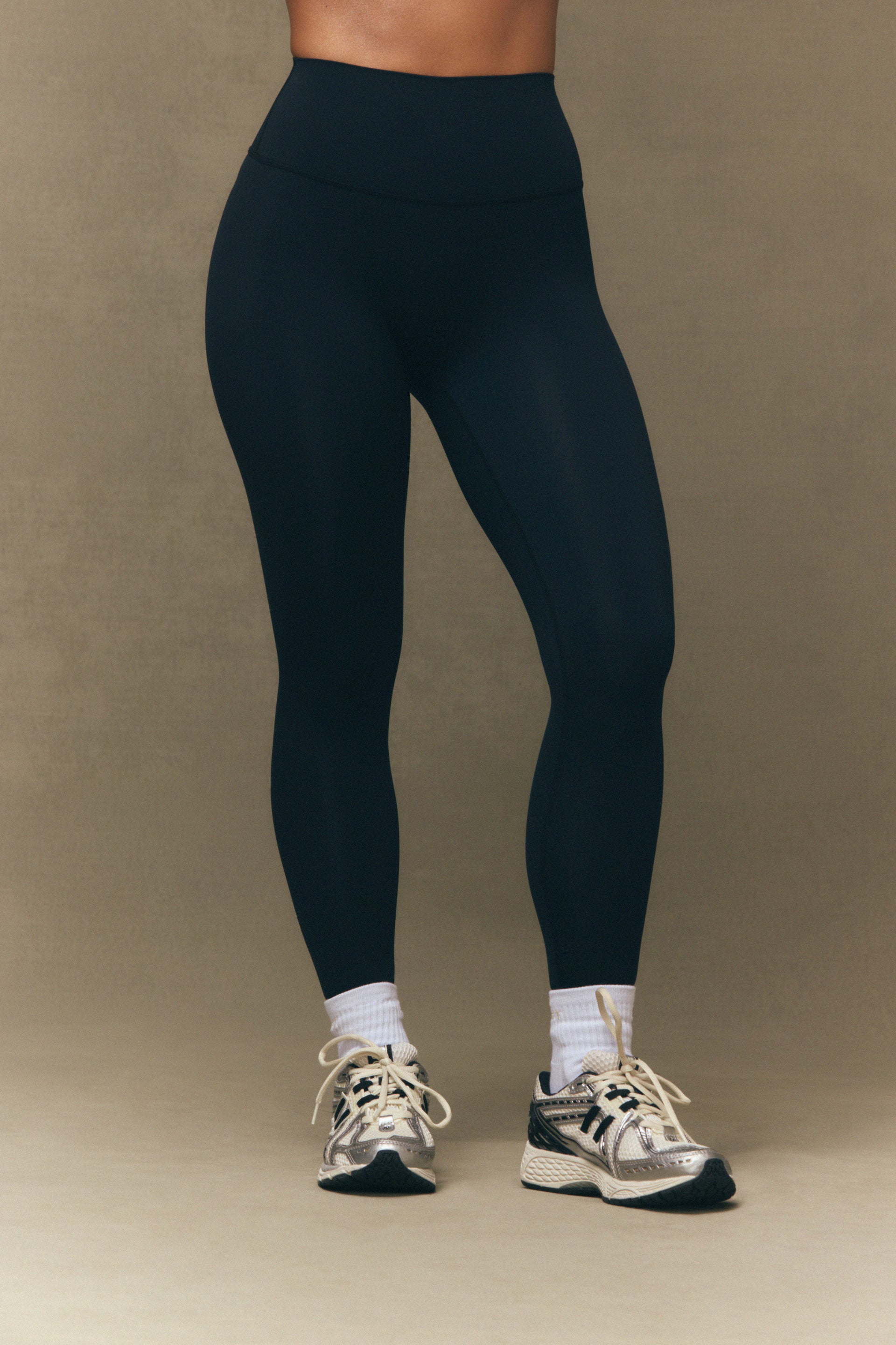 Person wearing black leggings and white sneakers on a beige background