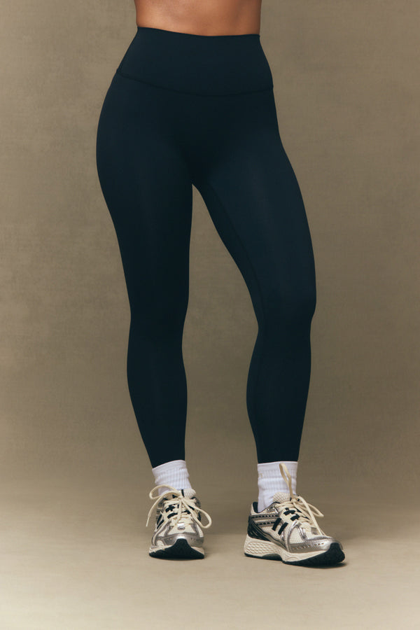 Person wearing black leggings and white sneakers on a beige background