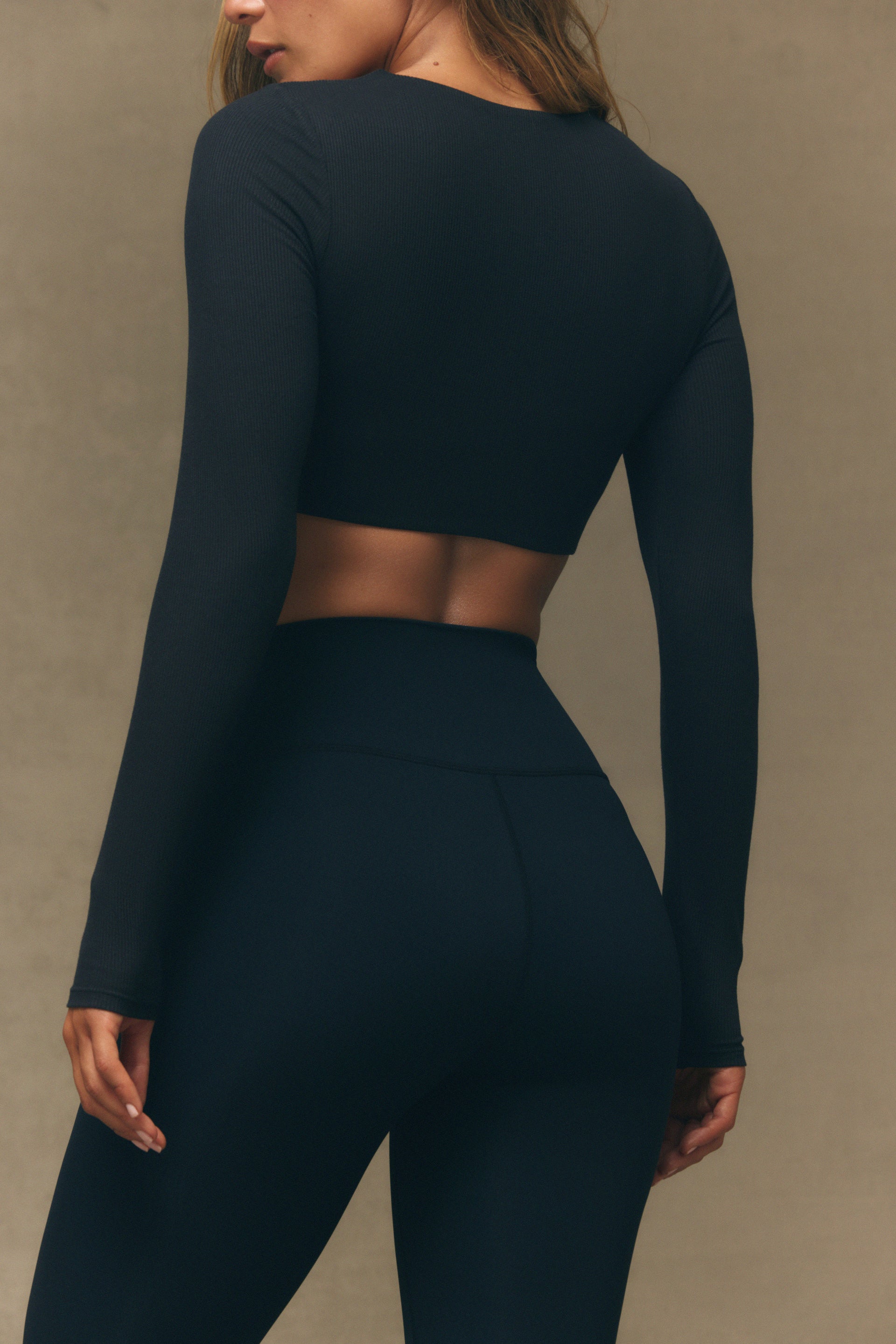 Person wearing a black long-sleeve top and leggings against a neutral background