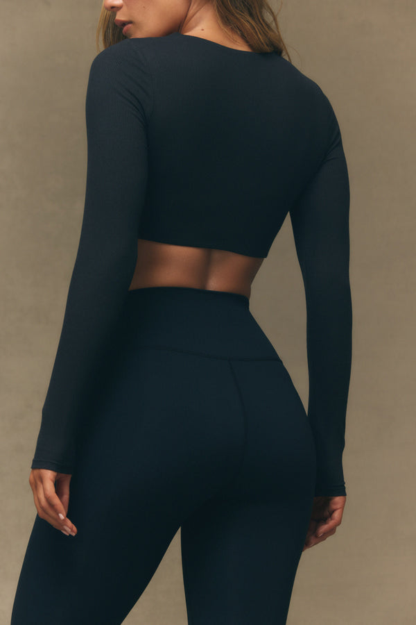 Person wearing a black long-sleeve top and leggings against a neutral background