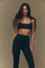 Woman wearing a black sports bra and leggings on a beige background <model-info>Jelene wears a size XS and is 5’7”, 23” waist, 32AB bust.</model-info>