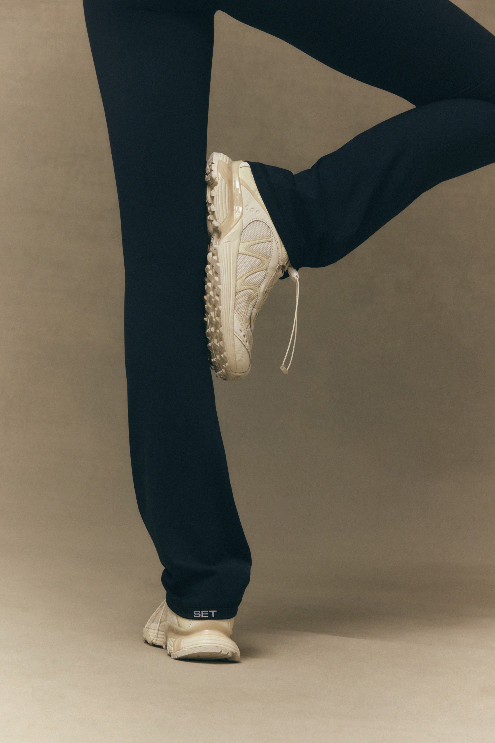 Person wearing black pants and white sneakers on a beige background