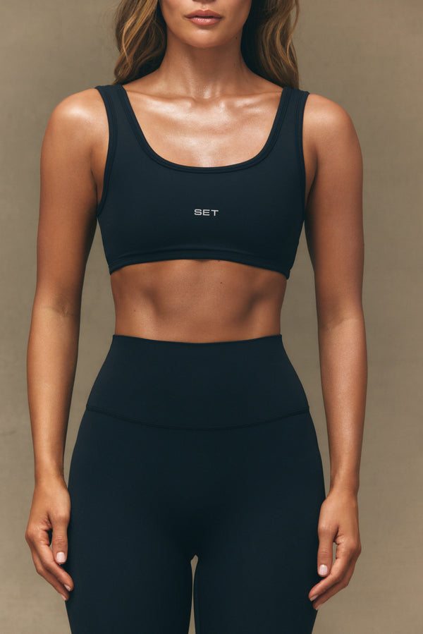 Person wearing a black sports bra and leggings with 'SET' branding on a beige background