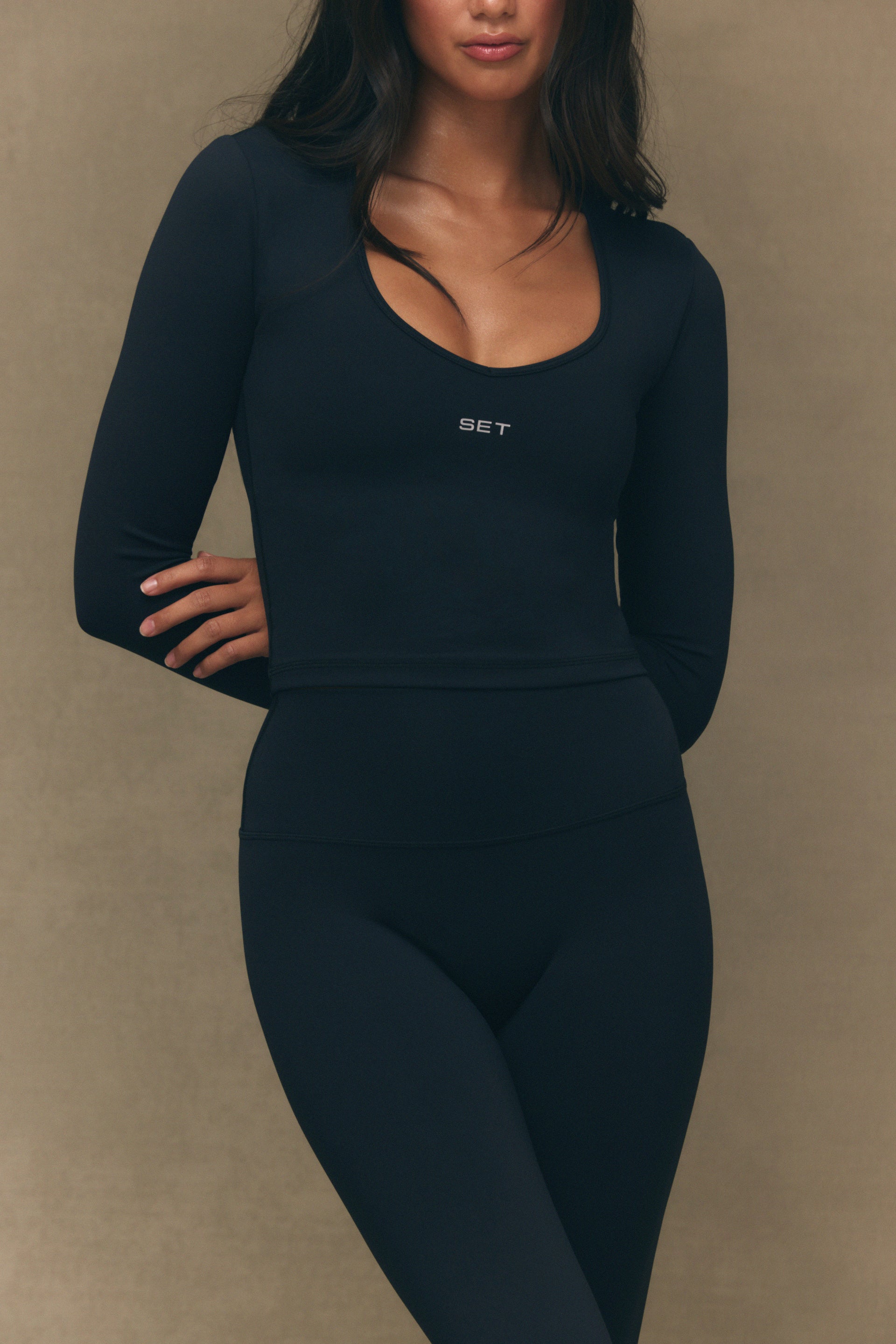Person wearing a black long-sleeve top and leggings with 'SET' branding on a beige background