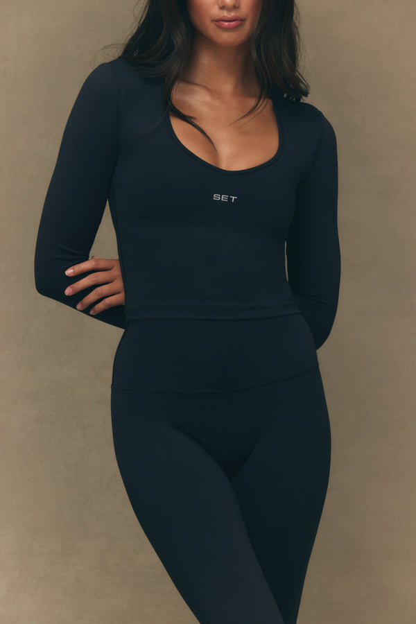 Person wearing a black long-sleeve top and leggings with 'SET' branding on a beige background
