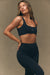 Woman wearing a black sports bra and leggings against a beige background <model-info>Bre wears a size S and is 5’7”, 25” waist, 32" bust.</model-info>