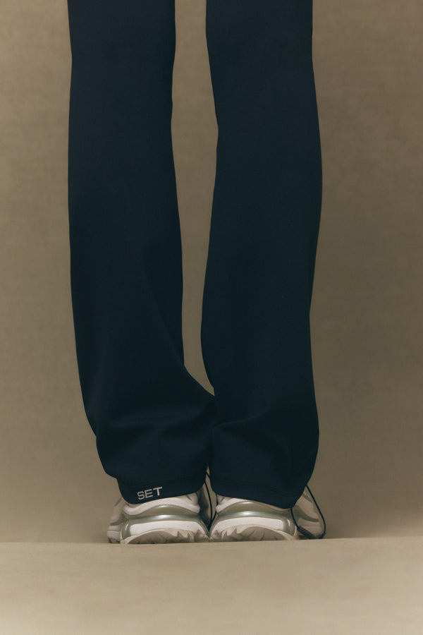 Black pants with a white logo worn by a person on a beige background