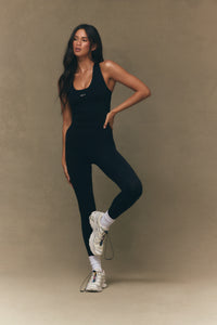 Woman wearing a black athletic outfit with white sneakers on a beige background 
