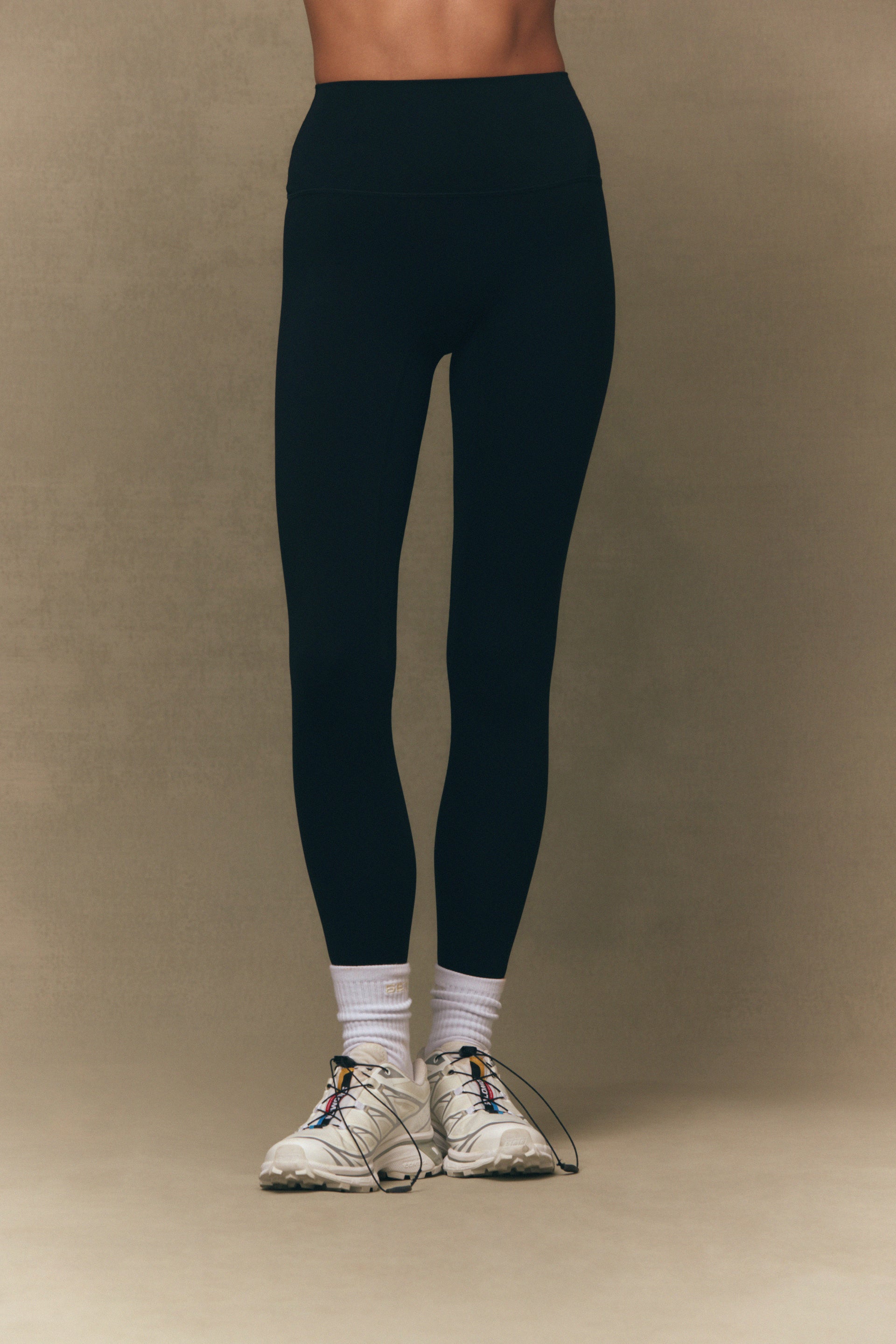 Person wearing navy leggings and white sneakers on a beige background <model-info>Jelene wears a size XS and is 5’7”, 23” waist, 32AB bust.</model-info>