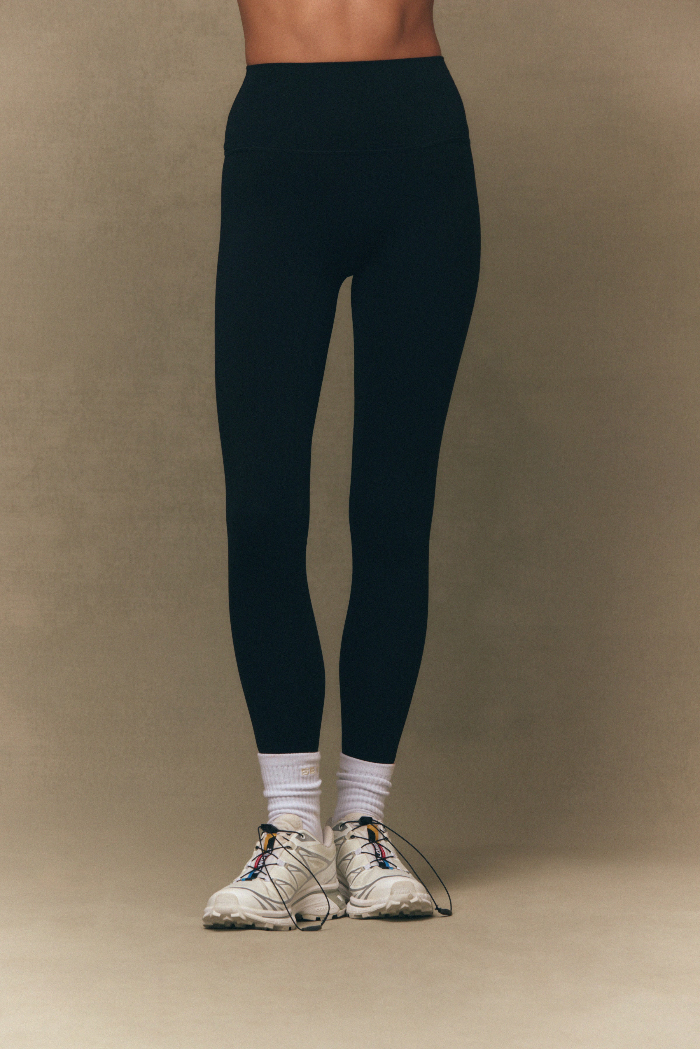 Person wearing navy leggings and white sneakers on a beige background 