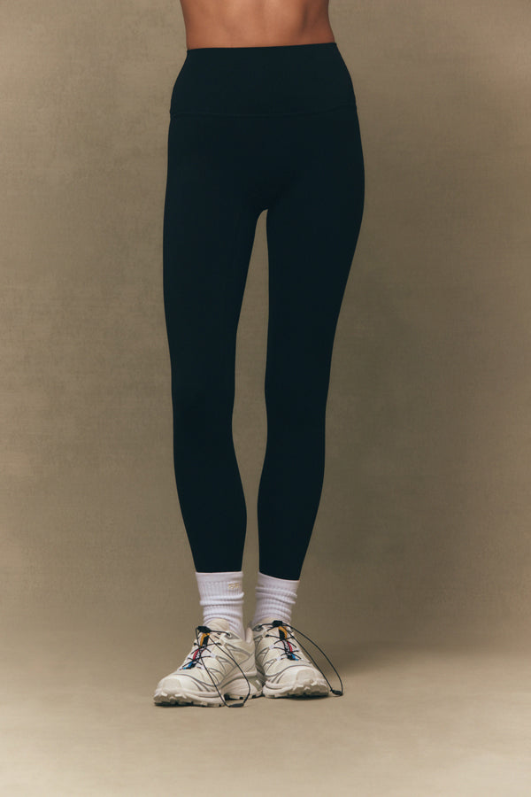 Person wearing navy leggings and white sneakers on a beige background 