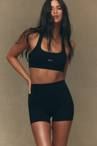 Woman wearing a black sports bra and shorts set against a beige background 