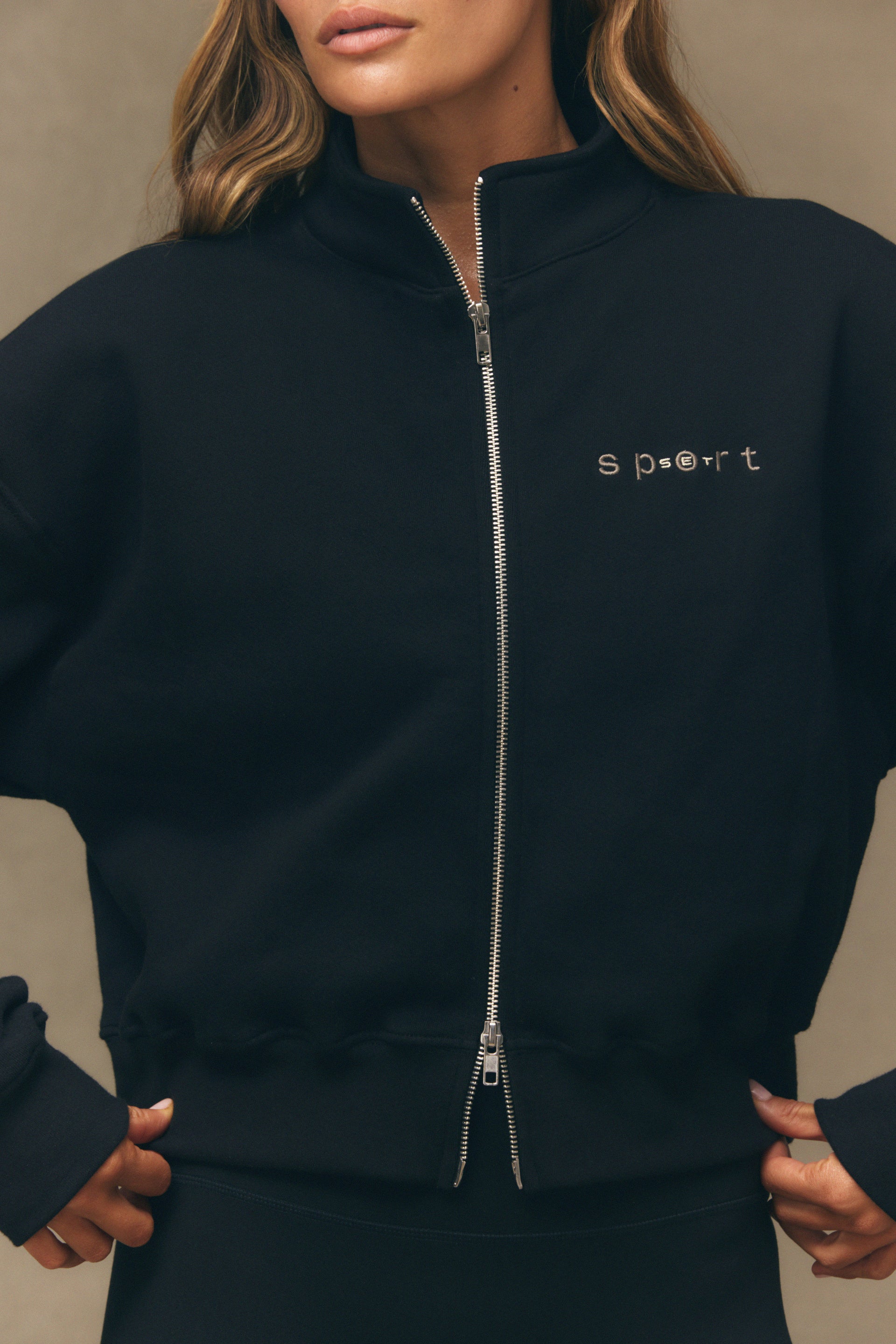 Black zip-up sweatshirt with 'sport' embroidery on a neutral background <model-info>Bre wears a size S and is 5’7”, 25” waist, 32" bust.</model-info>