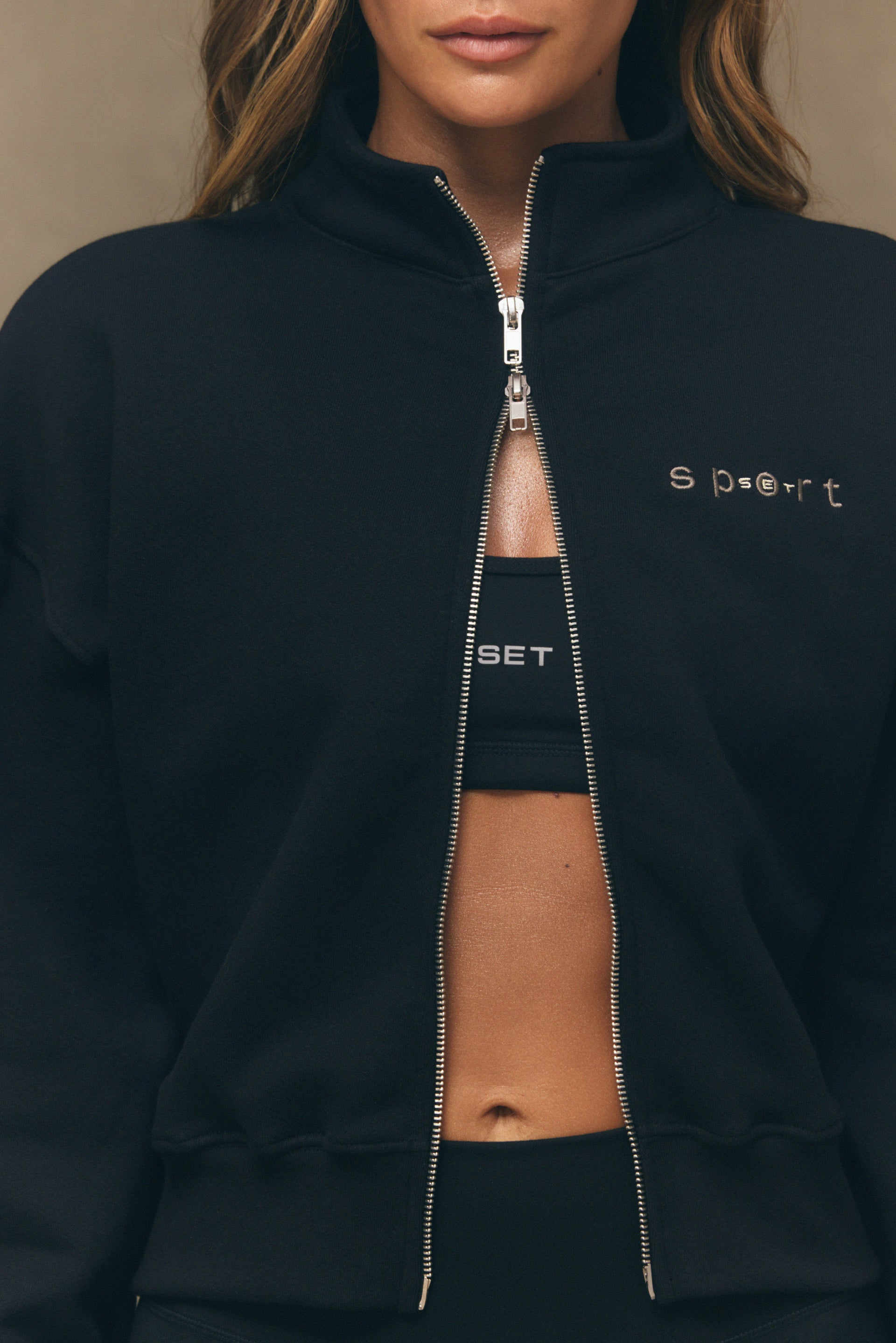 Person wearing a black zip-up hoodie with 'Sport' branding on a neutral background