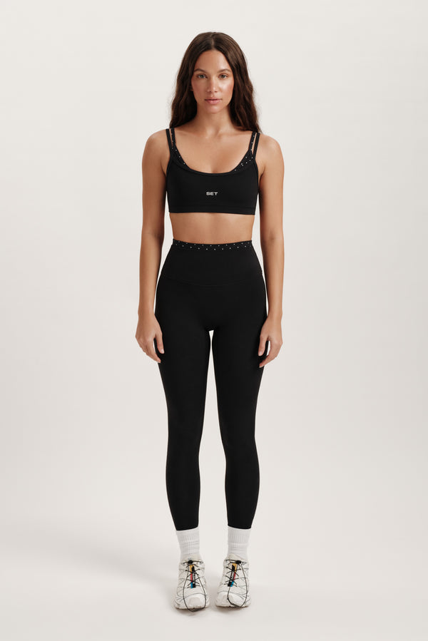 Woman wearing a black sports bra and leggings set on a white background