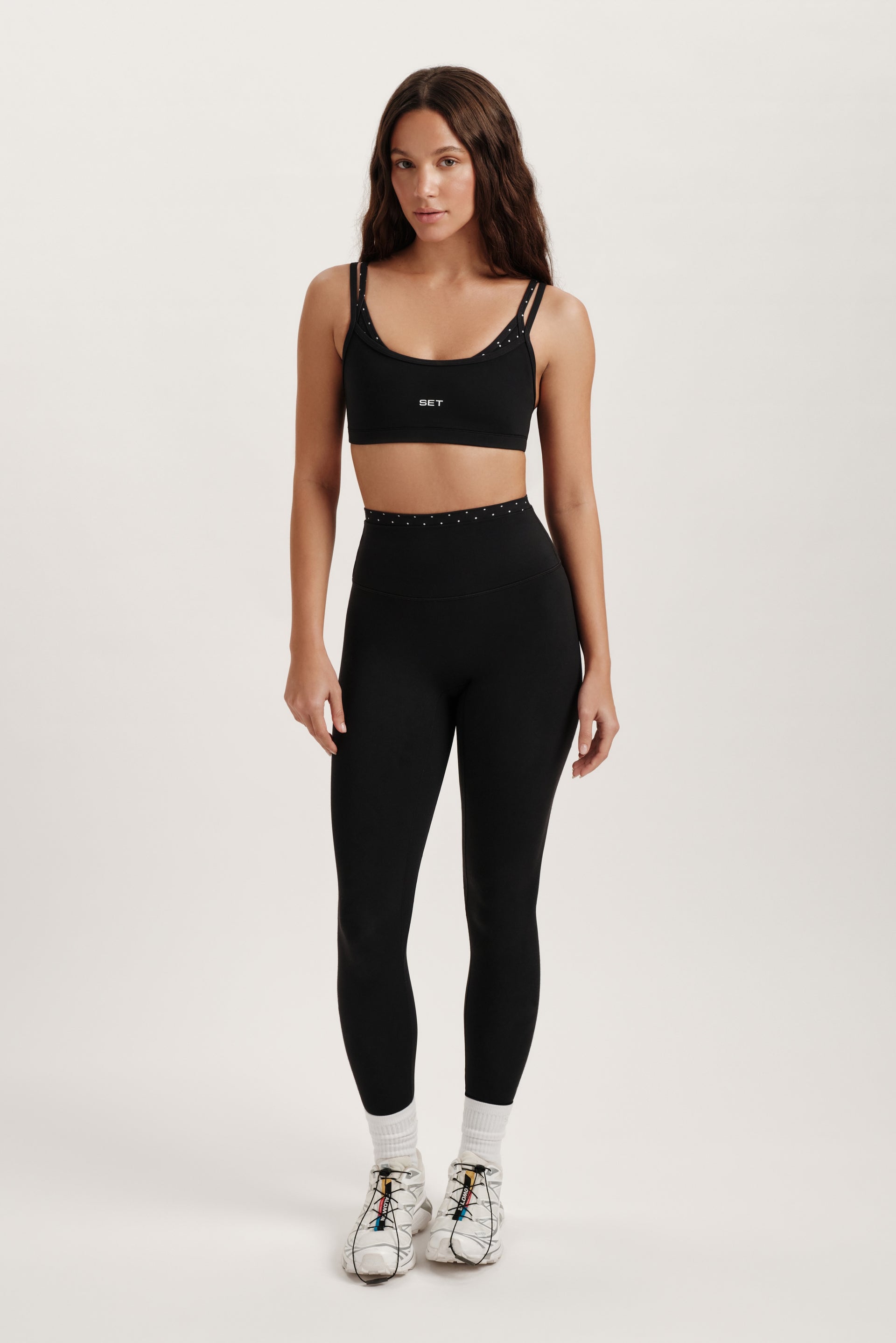 Woman wearing a black sports bra and leggings set on a white background