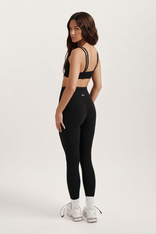 Woman wearing a black sports bra and leggings on a white background