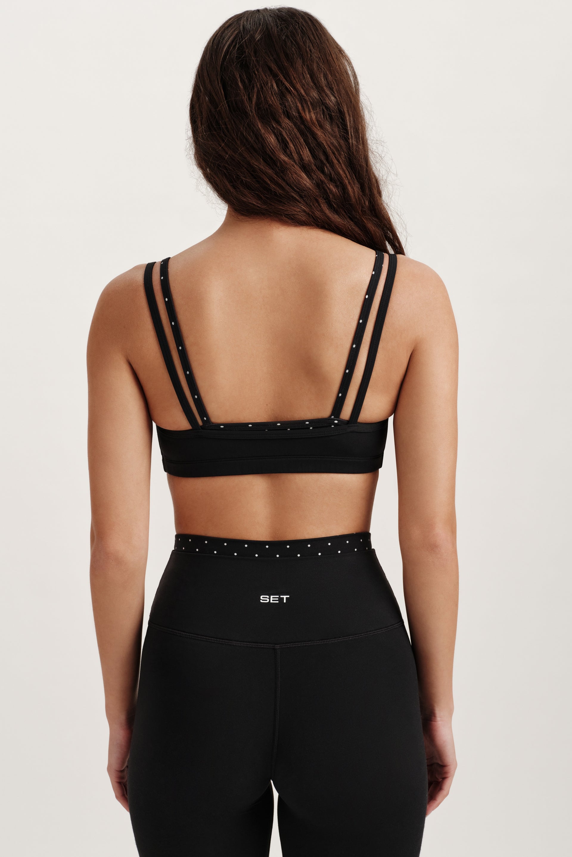 Person wearing a black sports bra and leggings with 'SET' branding on a light background